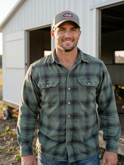 Travis, 36, Arkansas poultry farmer smiling near chicken houses in Washington County