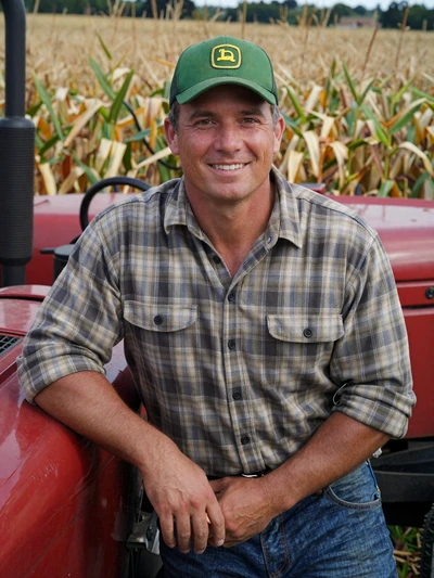 Dale, 46, Missouri mixed-operation farmer leaning against a tractor in Saline County with a cornfield behind him
