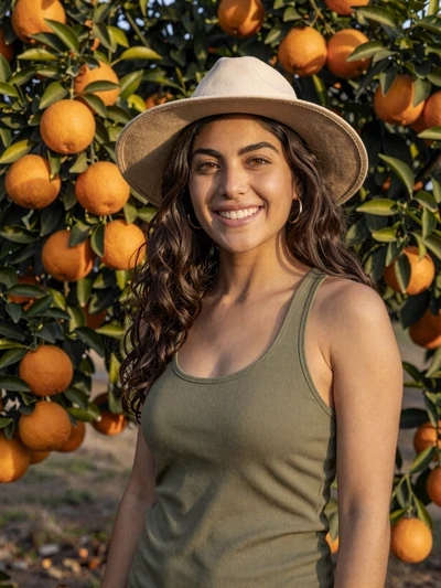 Sofia, 33, California citrus farmer smiling in orange grove in Riverside County golden light
