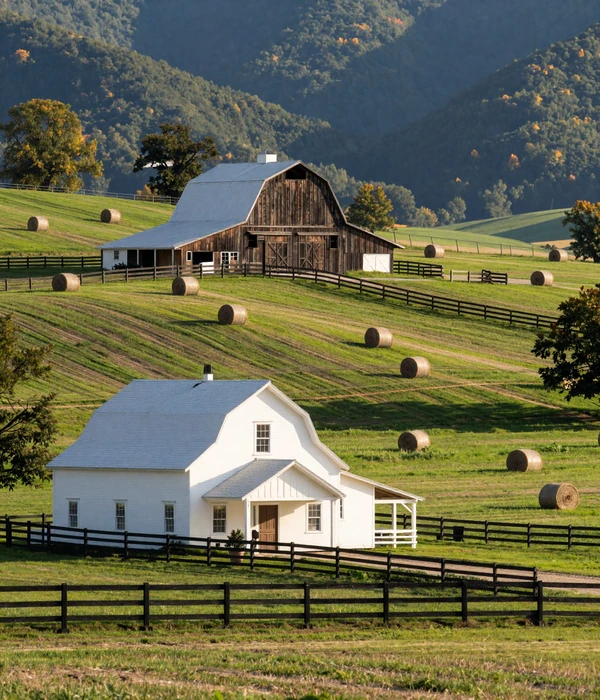 Tennessee farm landscape with white farmhouse, rolling green hills, hay bales, and a weathered tobacco barn against blue mountain ridges