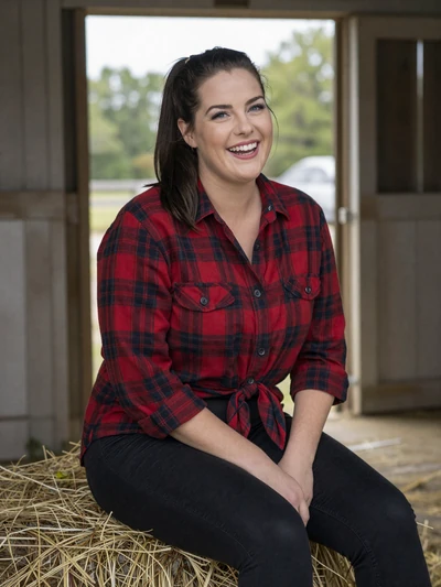 Jenna, 33, Iowa farmer sitting on a hay bale in a barn doorway with her golden retriever