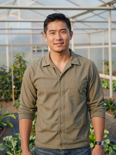 Kevin, a 38-year-old Chinese-American farmer smiling in front of a greenhouse on his California vegetable farm