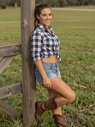 Kayla, a 28-year-old country woman from Missouri leaning against a fence in a green pasture wearing cowboy boots