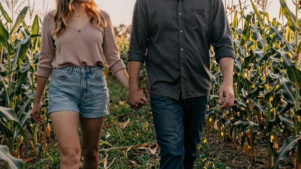Farming couple holding hands in a sunlit cornfield, complete guide on how to date a farmer
