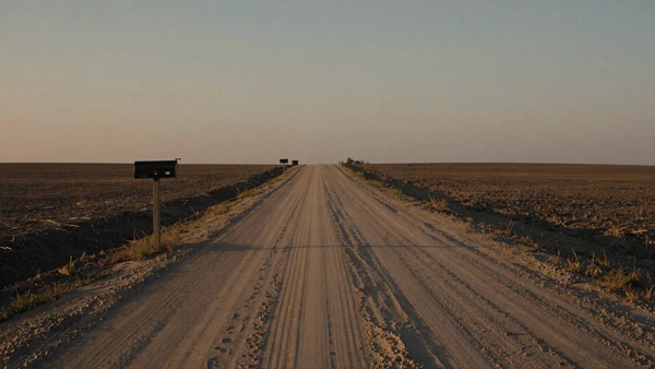 Empty rural dirt road stretching through flat farmland at dusk, rural dating challenges concept